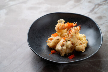 Expertly crafted tempura shrimp served on a sleek black plate, adorned with colorful garnishes. Enjoy a taste of exquisite European cuisine in an elegant dining setting