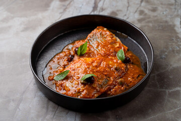 Indulge in a beautifully plated dish featuring tender fish smothered in a rich tomato sauce, garnished with fresh herbs