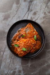 Deliciously prepared fish in a vibrant tomato sauce sits on a sleek black plate, with fresh basil leaves adding a pop of color. This European dish invites diners to indulge in flavorful cuisine