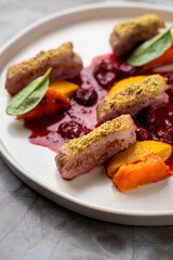A beautifully plated dish of succulent duck slices garnished with a crunchy pistachio crust, surrounded by colorful pieces of fruit and a rich sauce. Perfectly enhances the dining experience