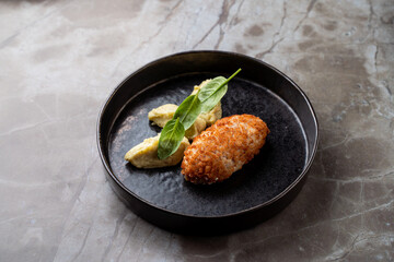 A beautifully plated European dish features a golden-brown croquette alongside creamy, flavorful...