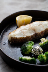 Succulent grilled fish garnished with lemon sits on a sleek black plate, accompanied by vibrant broccoli