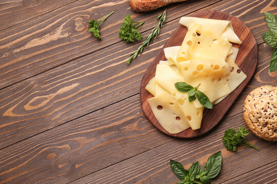 Board with tasty cheese slices and bread on wooden background