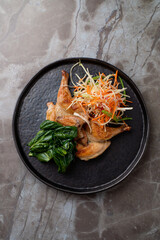 A delicious presentation of a European dish showcasing tender quail garnished with a colorful blend of fresh vegetables, resting on a sleek black plate