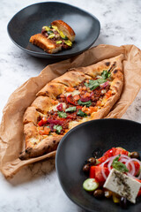 A cozy restaurant setting showcases an assortment of European dishes. A beautifully baked flatbread garnished with fresh herbs, accompanied by a vibrant vegetable salad and a delectable appetizer