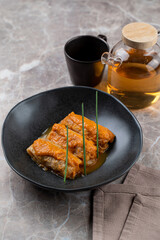 A beautifully arranged plate showcases a gourmet European dish, featuring tender meat drizzled with sauce, accompanied by fresh herbs. A tea pot and cup enhance the dining experience