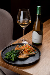 Indulge in a delightful meal featuring perfectly grilled fish served alongside vibrant vegetables and complemented by a crisp glass of white wine, all set in a cozy restaurant atmosphere