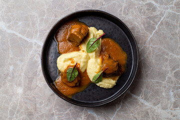 Savory pieces of succulent meat glazed with rich sauce rest on a bed of velvety mashed potatoes, complemented by fresh herbs, creating an exquisite dining experience in a chic European restaurant