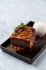 Savor the rich, velvety chocolate brownie adorned with a luscious caramel drizzle, accompanied by creamy vanilla ice cream, showcasing the artistry of European dessert-making
