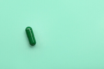 Green medical capsule on turquoise background