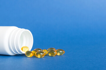 Soft gels pills with Omega-3 oil spilling out of pill bottle close-up. Gel capsules bottle white...