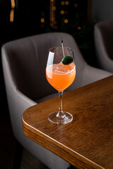 Elegant cocktail glass sits on a polished wooden table in a charming restaurant setting, surrounded by plush seating and ambient lighting, offering a delightful taste of European cuisine