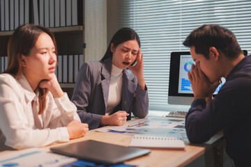 Asian businesspeople are feeling stressed and tired from work during a meeting in the office, analyzing financial graphs showing declining revenue and experiencing a business failure