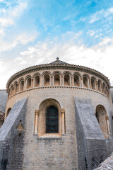 Obraz premium Ancient Romanesque church with arched windows and stone walls, featuring a stained-glass window, buttresses, and a blue sky