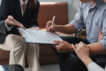 Businessman signing important legal document on clipboard while businesswoman explaining terms and...