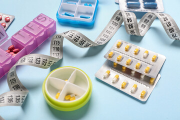 Containers, blister packs with weight loss pills and measuring tape on blue background