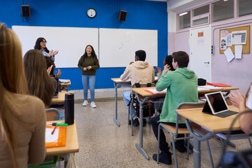 High school students applauding classmate giving presentation in classroom