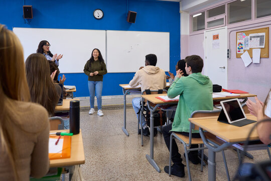 High school students applauding classmate giving presentation in classroom - Powered by Adobe
