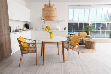 Interior of spacious stylish kitchen studio with table, armchairs, mimosa flowers, houseplant, counters and sofa