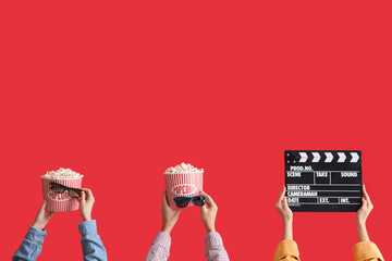 Many hands with buckets of popcorn, movie clapper and 3D glasses on red background