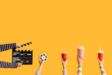 Many hands with movie clapper, bucket of popcorn and drinks on yellow background