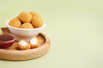 Wooden plate with delicious fried mozzarella balls and sweet sauce on green background