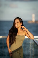 Young woman in a green dress poses on a balcony with a serene ocean backdrop during sunset.