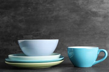 Stack of clean tableware and cup on table against black grunge background