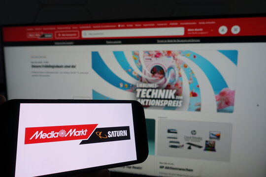 Kiel, SH, Germany March 19 2025 Smartphone with the logo of Media Markt and Saturn in front of a monitor showing their business website, highlighting promotions and offers