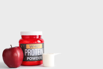 Bottle with protein powder and apple on light background