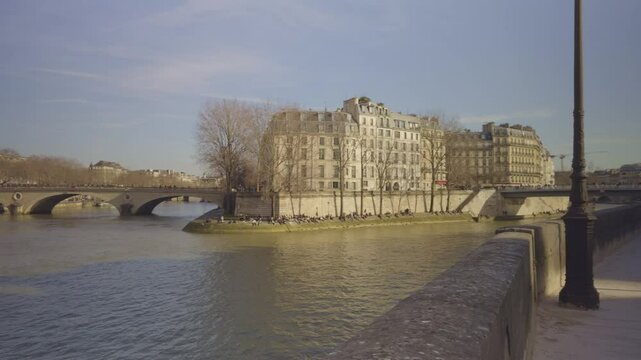 Seine River in Paris, historic stone bridge, people enjoying sunny winter day long shore. Panning