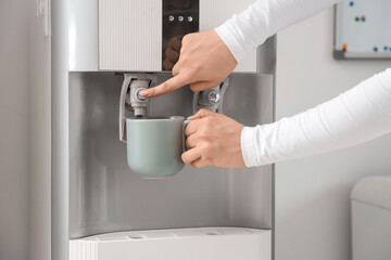 Female hands filling cup with filtered water from cooler in room