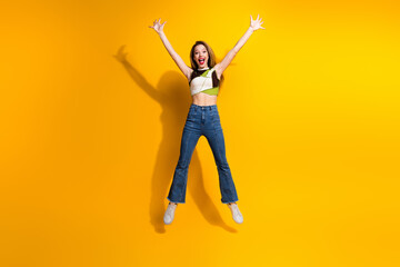 Excited Young Woman Jumping with Joy Against a Bright Yellow Backdrop, Expressing Happiness and...