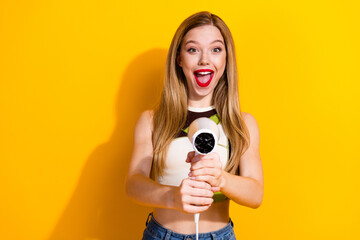 Obraz premium Happy young woman holding a hairdryer in colorful casual outfit against a bright yellow background