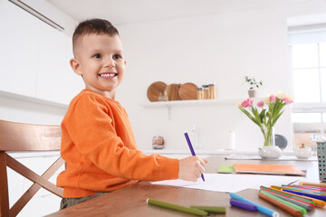 Naklejka premium Little boy drawing with felt-tip pens on table in kitchen