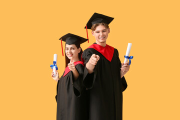 Happy graduate couple with diplomas on yellow background