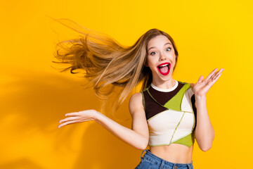 Excited young woman with beautiful long blonde hair posing against vibrant yellow backdrop in...