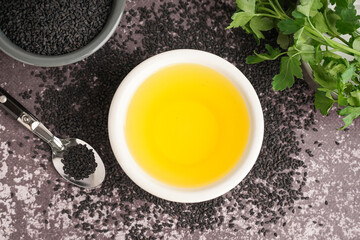 Bowl of oil with spoon, parsley and sesame seeds on grey grunge background
