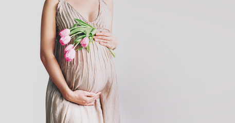 Beautiful pregnant woman with tulips flowers holds hands on belly. Young woman in dress waiting for...