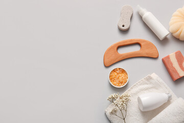 Composition with wooden guasha body massage tool, bottles of cosmetic products and towel on grey background