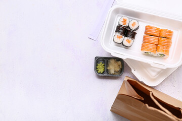 Plastic containers with tasty sushi rolls, marinated ginger and paper bag on lilac grunge background. Delivery concept