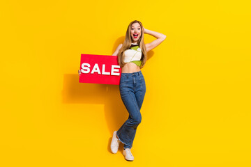 Youthful woman holding a sale sign in a playful pose against a vibrant yellow background, capturing...
