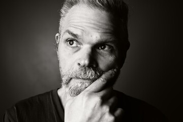 Portrait of mature caucasian man with hand on chin looking thoughtfully to the side. Black and...