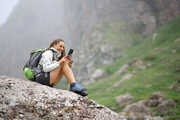 Happy hiker using smart phone sitting on a rock in nature