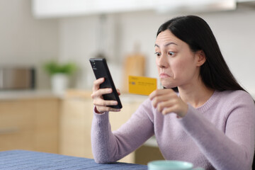 Perplexed asian woman paying online in the kitchen