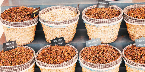 A selection of coffee beans from various origins displayed in woven baskets at a market. The mix of roasted and raw beans highlights the global diversity and trade of coffee.