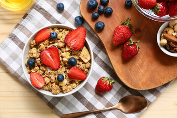 Wooden tray, napkin, bowl with tasty granola and berries on yellow wooden background