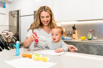 Happy mother helping baby boy drawing with dot markers at home