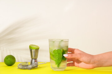 Woman taking glass of fresh mojito from yellow table on white background