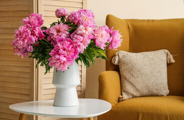 Vase with peonies flowers on coffee table near armchair in living room, closeup